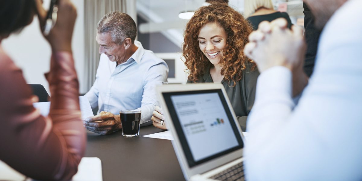 Smiling young businesswoman sitting with a diverse group of work colleagues during a meeting in an office boardroom